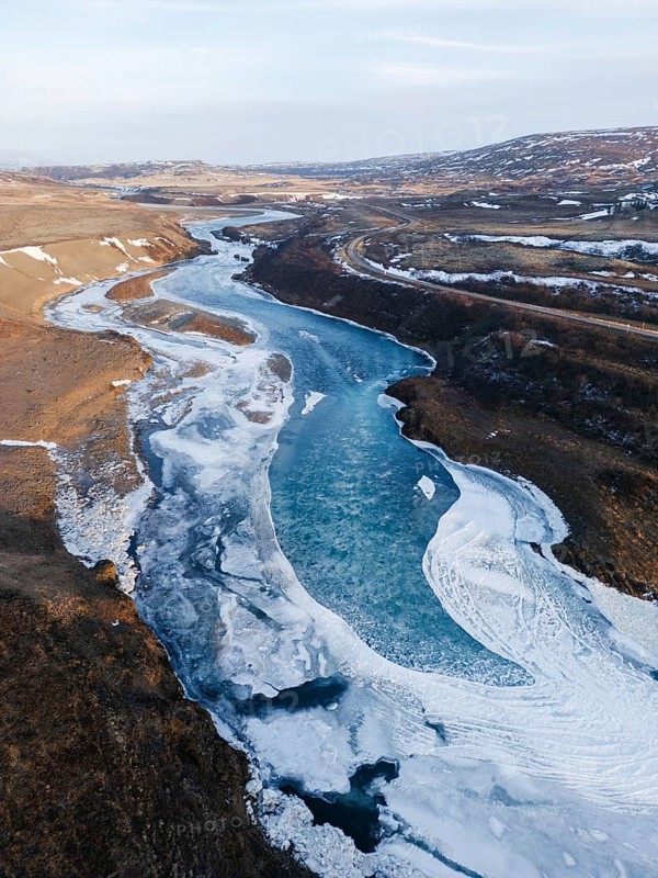 Aerial view of a frozen river curving through the rugged Icelandic terrain. Snow and ice blanket the wild, remote landscape under a cold, pale winter sky, Selfoss, SuÃ°urland, Islandia