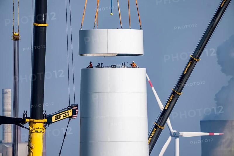 Construction site of the new Bedburg 3 wind farm, on recultivated open-cast mining site, 9 wind power plants with an output of 60 megawatts are newly built, installation of the wind turbine tower, in the background the Neurath lignite power plant, operated by RWE and the city of Bedburg, North Rhine-Westphalia, Germany