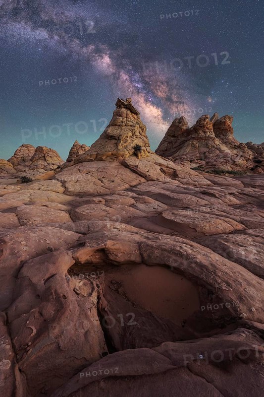 Stunning view of the Milky Way stretching across a starry night sky, above rugged, rocky desert formations in Coyote Buttes, Arizona. Captures the beauty and mystery of nature