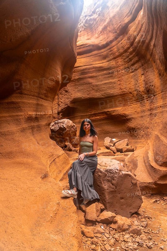 Young woman sitting on a rock, enjoying the breathtaking view of barranco de las vacas canyon in gran canaria, spain