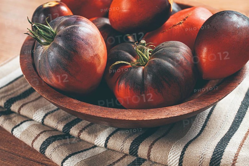 Freshly picked tomatoes, of the Black Beauty variety, in a wooden bowl, close-up, on the kitchen table