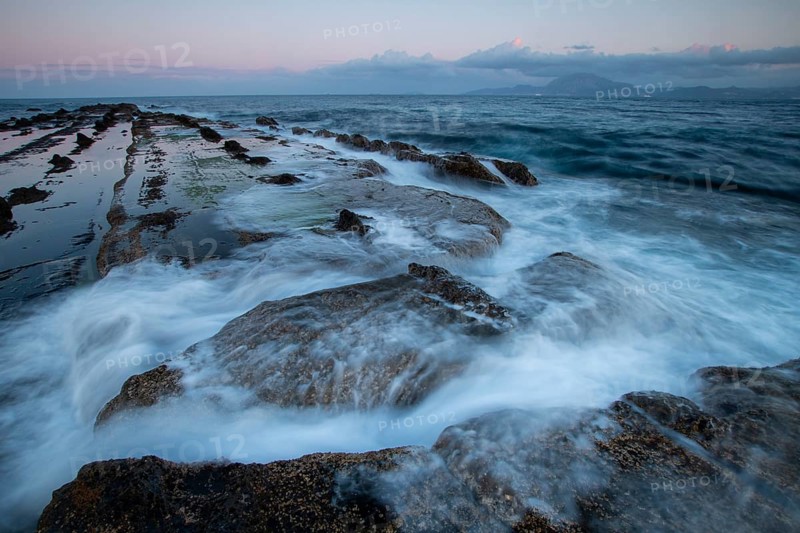 Serene sunset over the rocky coastline of Tarifa, Cadiz. Waves gently crash over the rugged rocks, creating a beautiful seascape in the soft evening light