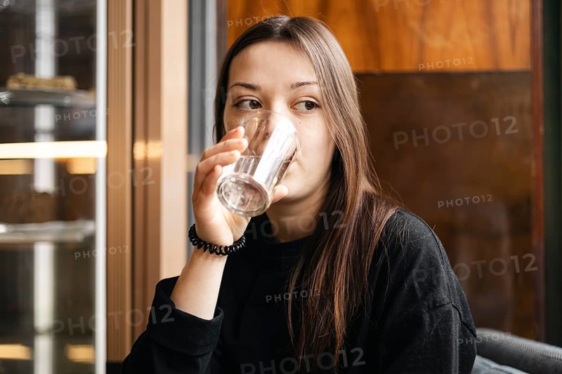 A young woman enjoys a glass of water while seated in a cozy cafe, exemplifying a casual, relaxing moment