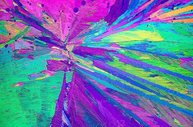 Close-up view of Adipic acid crystals under a microscope, showcasing a vibrant spectrum of purple, pink, green, and blue hues