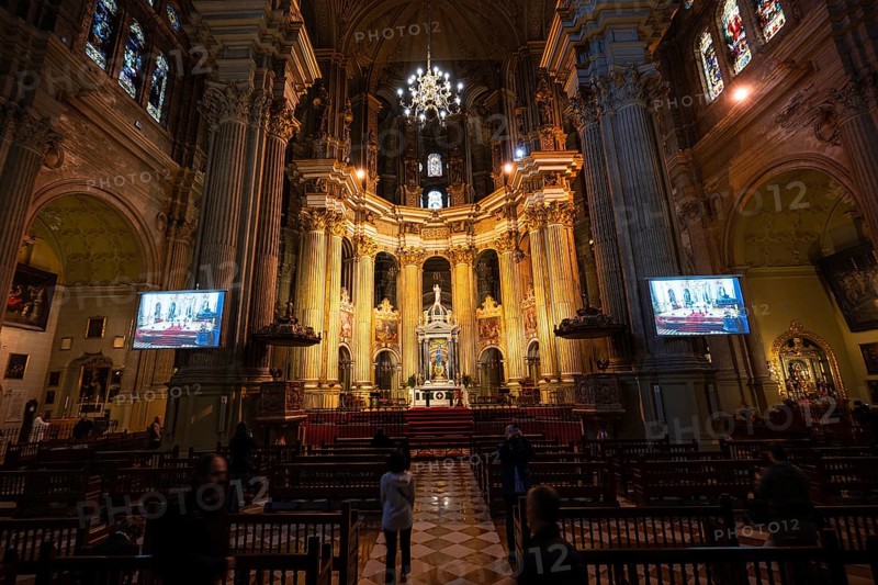 MALAGA, SPAIN - FEBRUARY 1, 2026: A wide interior panorama of Malaga Cathedral's nave and apse during a service, with lights on, high vaults, and a few people in pews