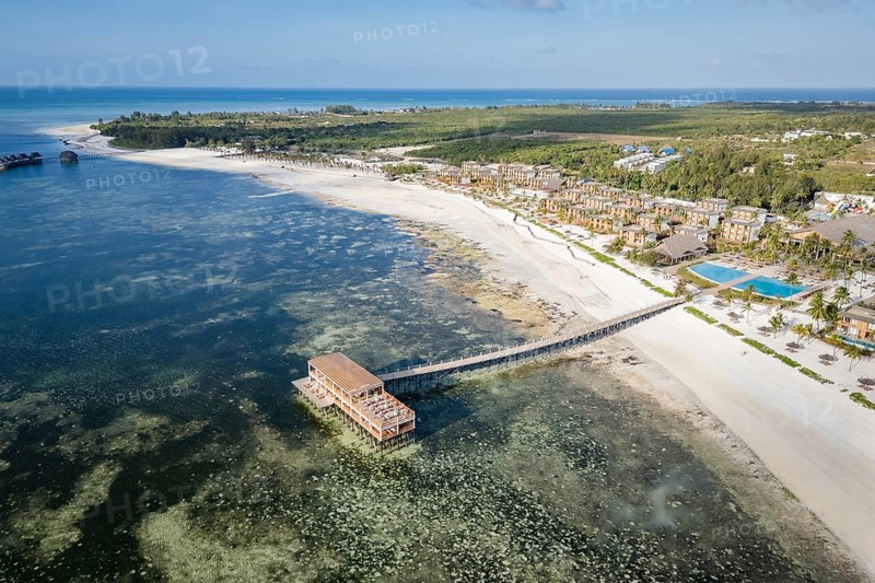 High angle aerial view of a luxury tropical resort on a white sand beach with a long wooden pier over turquoise ocean water in Zanzibar, Tanzania