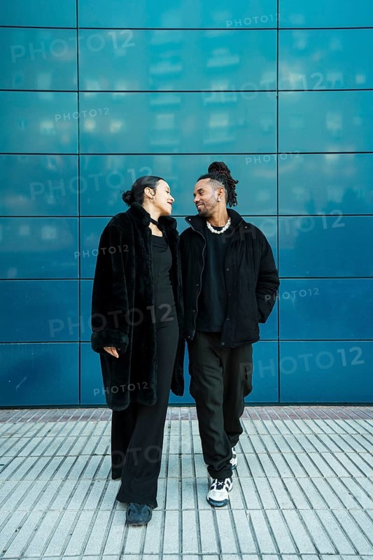 A multicultural couple walks closely, showcasing diversity and unity. The man and woman share a joyful moment against a modern blue background, embodying multiethnic harmony