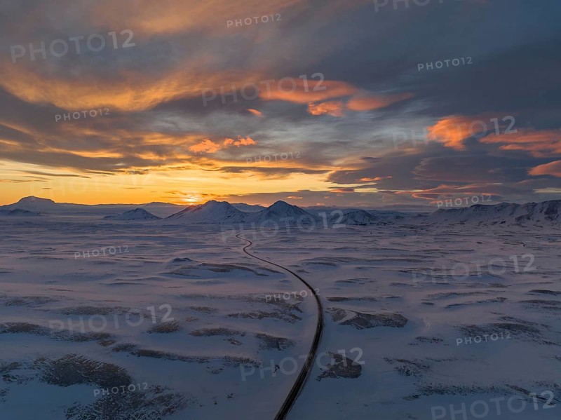 Stunning winter sunset over Iceland's snow-covered expanse, featuring dramatic skies and a winding road leading towards distant mountains
