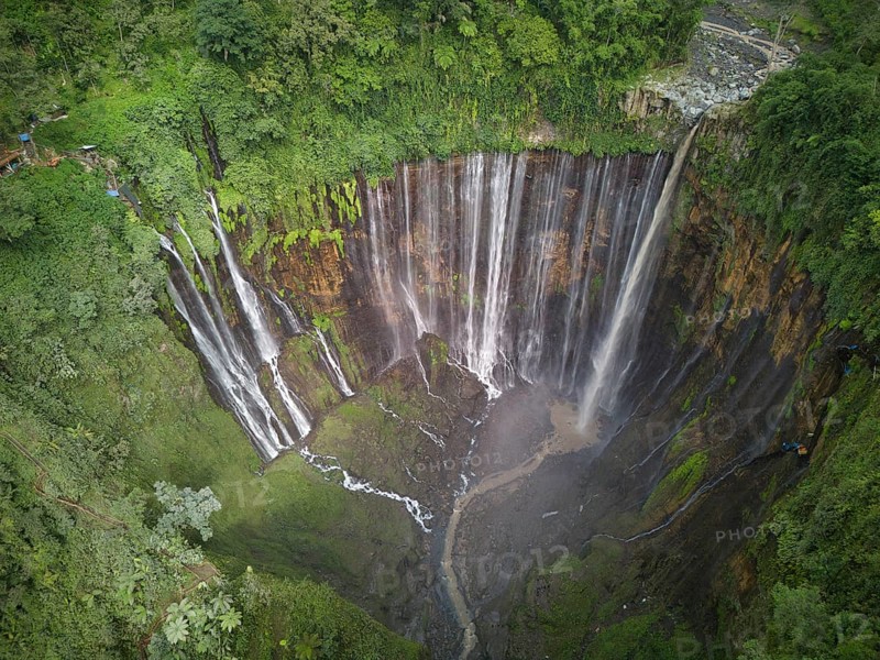 An aerial shot captures the stunning Tumpak Sewu Waterfall in full glory, showcasing multiple cascades over lush green cliffs