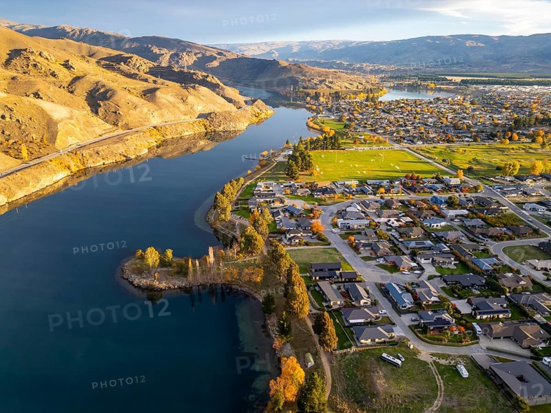 Aerial view of Queenstown during autumn, showcasing vibrant foliage and a lake, stunning landscapes. The drone captures a serene blend of urban and natural beauty under golden light