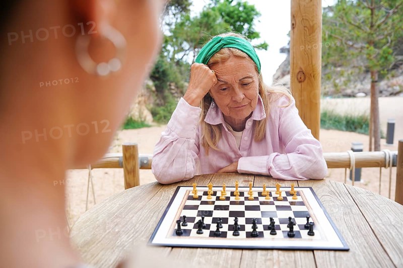 Mother and daughter plays chess on a wooden table in a serene outdoor park Focused and thoughtful, she enjoys a peaceful game surrounded by nature A relaxing leisure activity