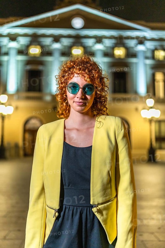 Woman with curly hair in elegant casual clothes standing in the city at night