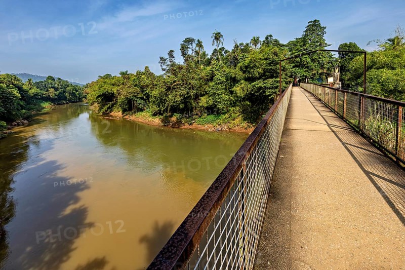 A bridge crosses a river surrounded by forest and clear skies, bridge over the Kalu River in Ratnapura in Sri Lanka