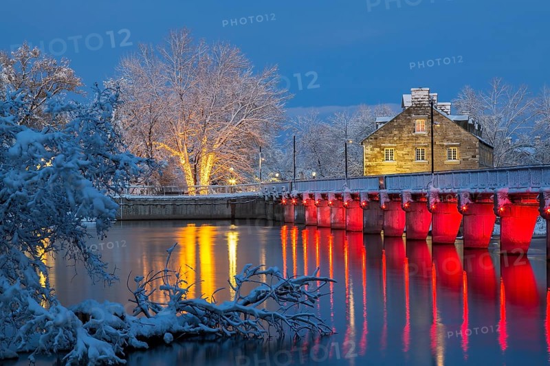 Illuminated Moulin Neuf water flow control dam and walkway over Des Mille-Iles river plus New Mill on Ile des Moulins with first winter like snow in late autumn at dusk, Old Terrebonne, Quebec, Canada
