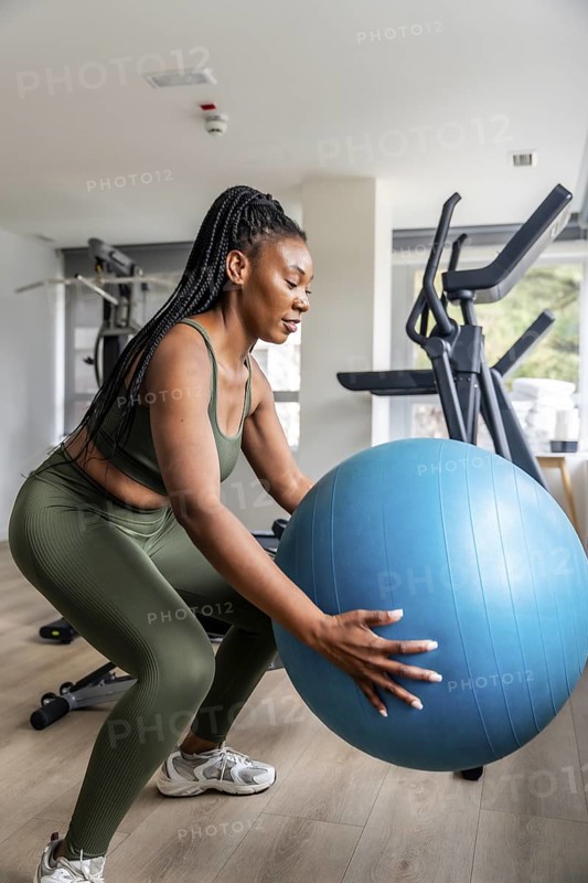 Concentrated businesswoman exercising with fitness ball in hotel gym during business trip, maintaining healthy lifestyle