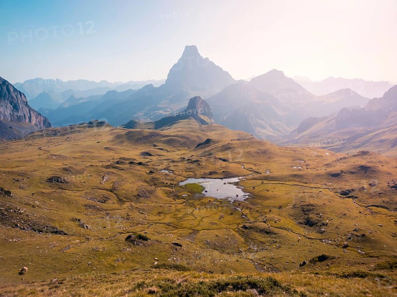 Scenic view of a tranquil mountain landscape with a prominent peak and expansive green valley, bathed in soft sunlight, conveying serenity and natural beauty in the Pyrenees