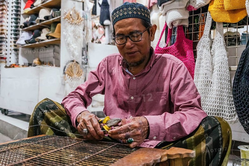 A balinese artisan skillfully repair at a vibrant market stall. Surrounded by handmade goods, his concentration and craftsmanship are evident
