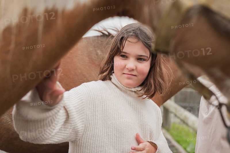 A young girl in a cozy sweater gently touches a horse on a sunny farm day. The scene captures the beauty of nature and the bond between the girl and the horse
