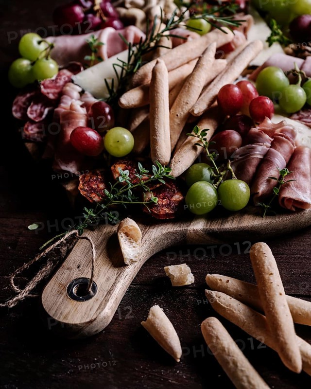 An enticing charcuterie board filled with a variety of snacks, including breadsticks, cured meats, cheeses, and fresh grapes, perfect for sharing and entertaining