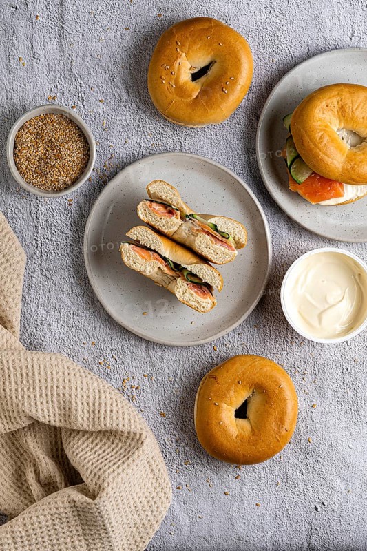 Top view of a selection of bagels with smoked salmon, cream cheese, and toppings. Bagels are displayed on plates with a textured cloth background, creating an appetizing scene
