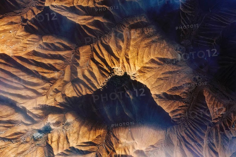 Aerial view showcasing a rugged desert landscape with intricate patterns and deep shadows Sunlight highlights the ridges, creating a dramatic and textured scene from above
