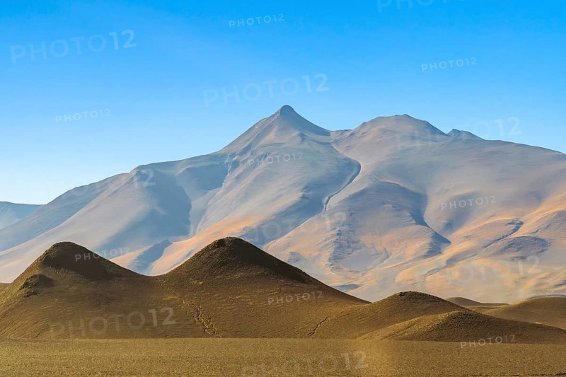Soft light illuminates the serene La Puna highlands in the South American Andes, showcasing the smooth, undulating silhouettes of the mountain peaks