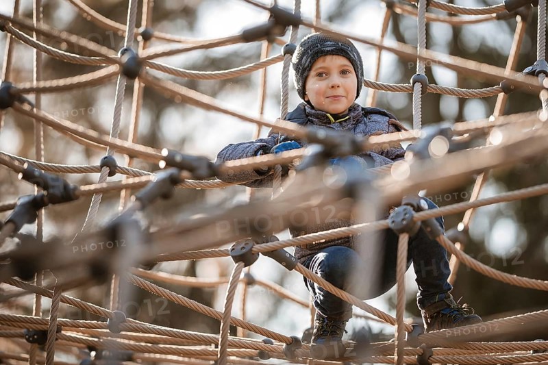 Cute boy in winter clothes on a rope construction at the playground