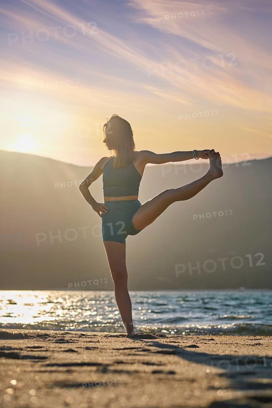 Yoga pose Utthita Hasta Padangusthasana Extended Hand-to-Big-Toe Pose at sunset on the beach