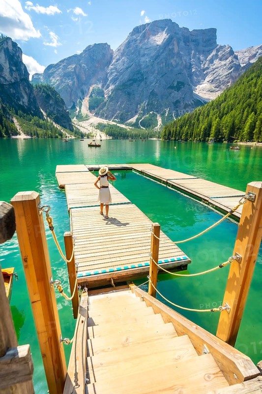 Tourist walking on a wooden pier at lake braies, also called pragser wildsee, with the seekofel mountain in the background, in the dolomites, italy