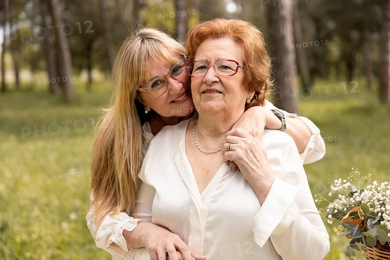 A loving moment between mother and daughter as they embrace in a sunlit park. The daughter lovingly holds her mother, showcasing family bonds and warmth on a sunny day
