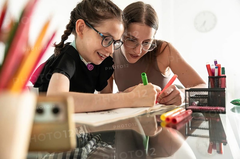 A heartfelt image of a sister supporting a disabled girl with a tracheostomy during a creative activity