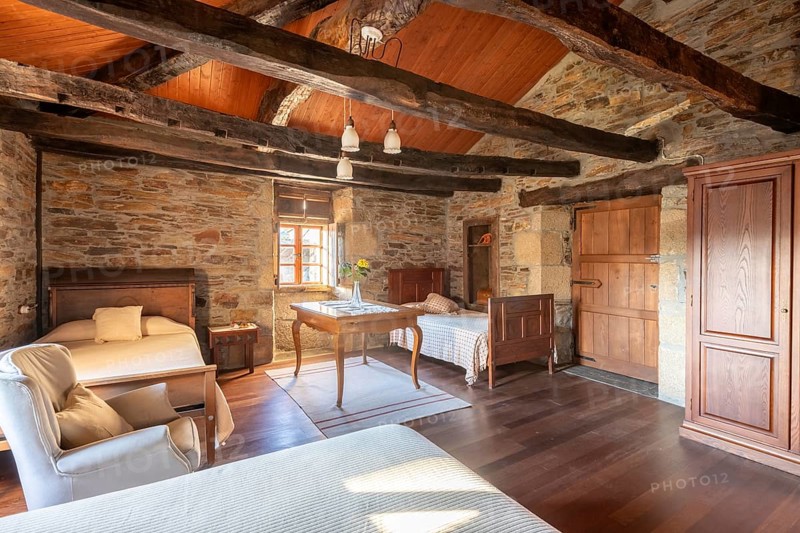 Charming, rustic bedroom interior featuring stone walls, wooden beams, and vintage furniture, located in a traditional country house in Lugo, Spain