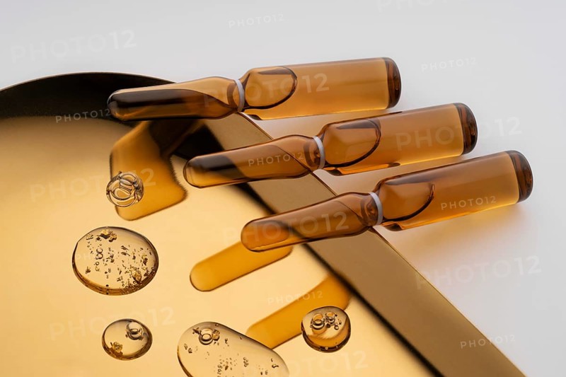 Elegant golden ampoules filled with anti-aging serum, strategically placed on a reflective surface to emphasize their sleek design and luxurious appeal