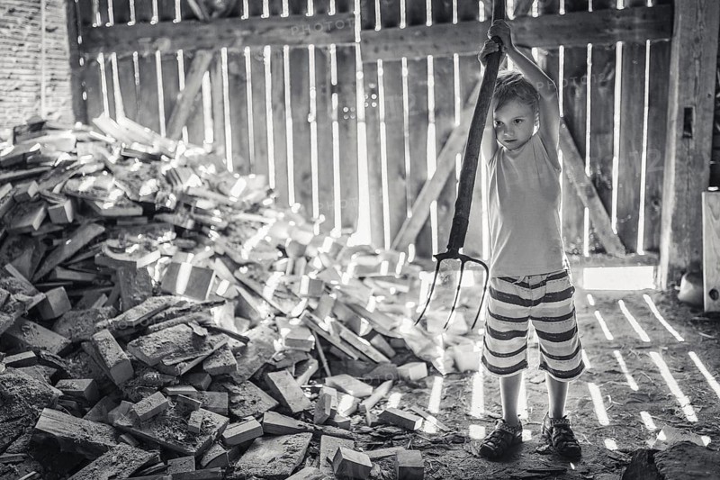 Little boy working in a shed with pitchfork
