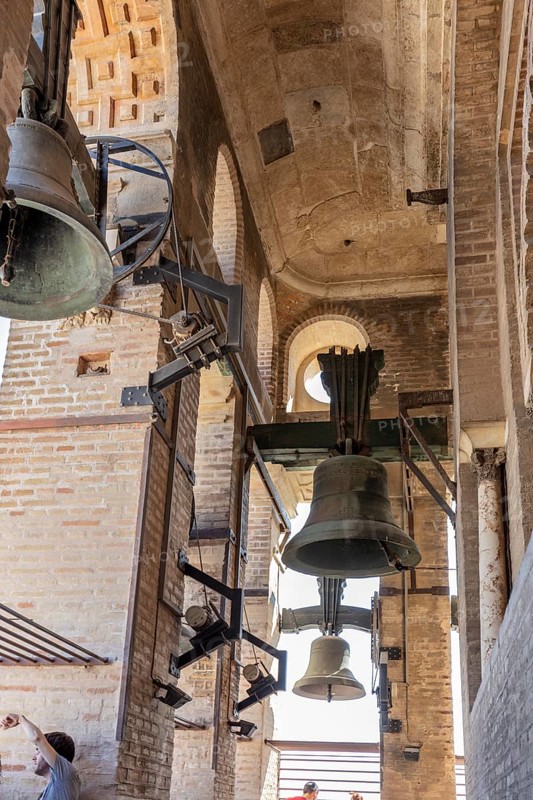 View into a historic bell tower with large bells and old brick walls, Seville