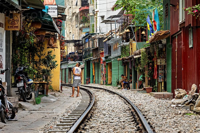 Railway line through a lively street with colourfully painted houses and a pedestrian, The Train Street of Hanoi Vietnam