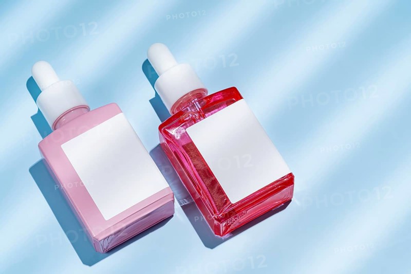 Top view of two cosmetic serum bottles in pink and red colors, positioned on a vibrant blue background with subtle-shadow effects, reflecting a minimalistic and modern aesthetic
