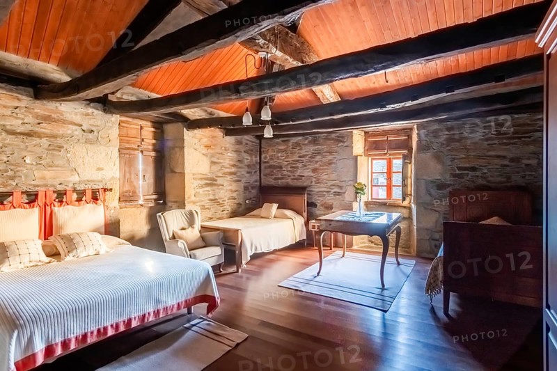 Cozy bedroom featuring rustic charm with wooden beams and stonework in a traditional country house located in Lugo, Spain. The warm lighting complements the natural materials used throughout