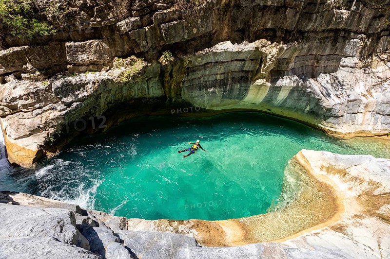 A canyoneer floats peacefully in a vibrant turquoise pool surrounded by curved canyon walls in Matacanes, Nuevo Leon, Mexico. A moment of calm in an adventurous setting