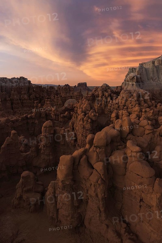 Breathtaking view of unique sandstone formations under a vibrant sunset sky at Goblin Valley State Park, Utah. The surreal landscape showcases nature's sculptural artistry