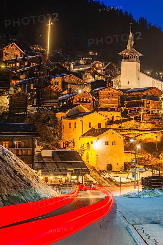 Braking track of a passing vehicle, old farmhouses and barn storage in the back, white cellars, the illuminated cross and the illuminated church tower of the Saint Theodule church, night view, historic town center, Grimentz, Val d'Anniviers, Valais Alps, Canton of Valais, Switzerland