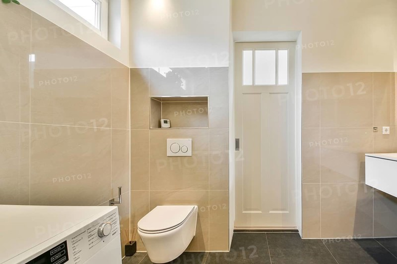 Stylish minimalist bathroom featuring neutral beige tiles, a wall mounted toilet, and sleek design elements. A washing machine is subtly integrated for functionality