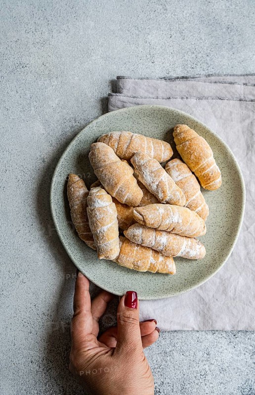 Top view of a plate filled with homemade pastries, held by a cropped unrecognizable woman's hand. The pastries are dusted with flour, enhancing their rustic and delicious appearance