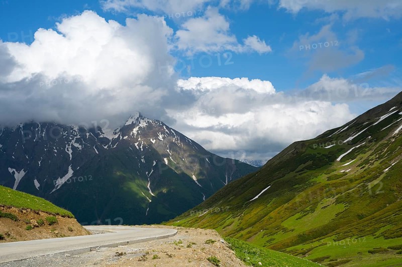 Road leads through mountains with clouds, blue sky and snow-capped peaks, Zagari Pass, Svaneti, Greater Caucasus, High Caucasus, Georgia