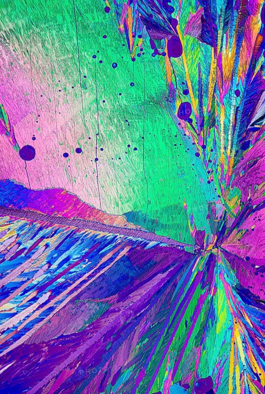 Vivid and colorful polarized light microscopy image of Adipic acid, crystals showcasing vibrant hues of pink, green, blue, and purple with dynamic textures and abstract forms