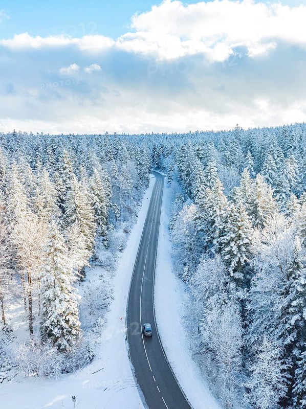 A narrow road crosses a quiet, snow-covered forest under a blue sky, Bad Wildbad, district of Calw, Black Forest, Germany