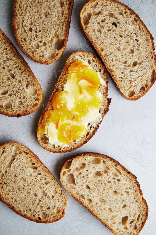 Top view of freshly sliced homemade sourdough bread topped with butter and jam, served on a textured surface