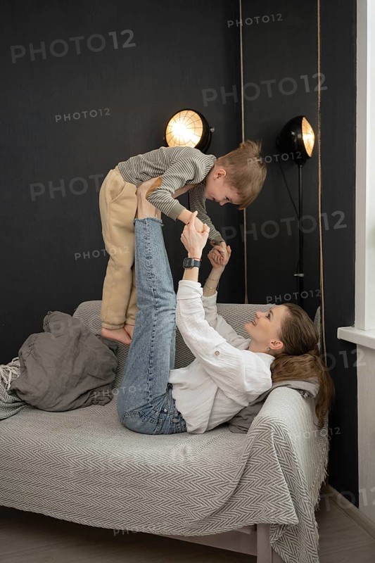 A mother joyfully plays with her young child on a couch. The room is warmly lit, creating a cozy and intimate atmosphere that emphasizes family connection and love