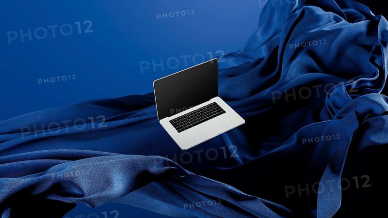 A sleek laptop is placed atop smooth fabric, showcasing its lightweight design against a rich blue backdrop