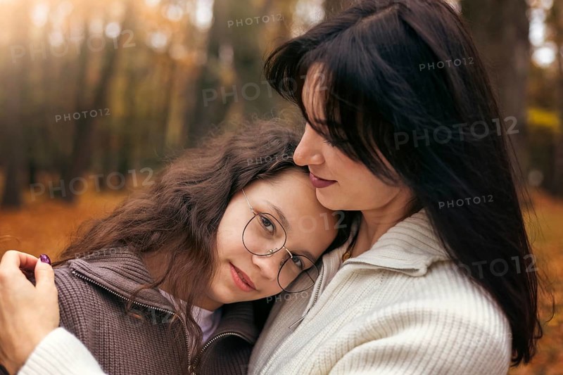 A mother lovingly embraces her daughter in an autumn forest, surrounded by golden leaves. The warm colors create a serene and heartwarming atmosphere, highlighting family bonds
